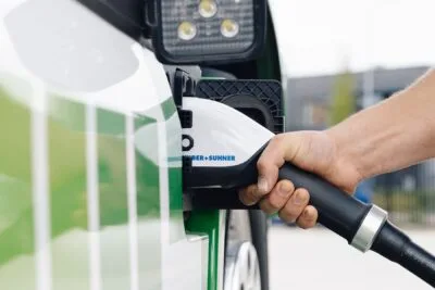 A human hand connects a charging cable into the charging port of an electric vehicle